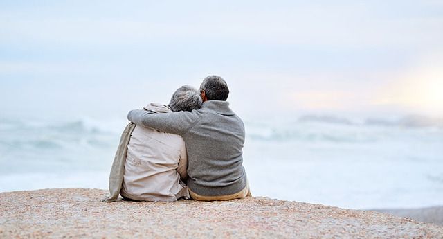 Eldre dame og mann som sitter på stranden og holder rundt hverandre.