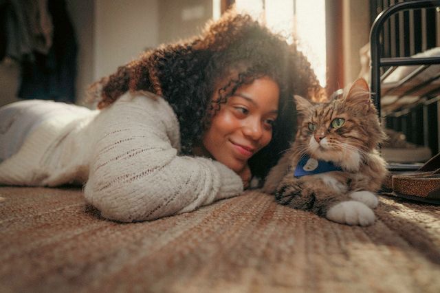 Jente som ligger på gulvet ved siden av en katt