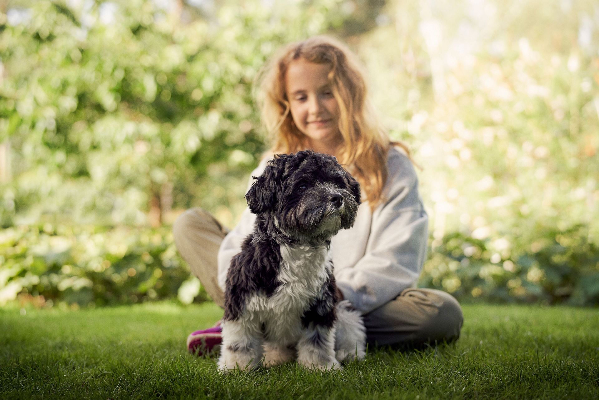 Jente sitter ute på gresset med hunden sin