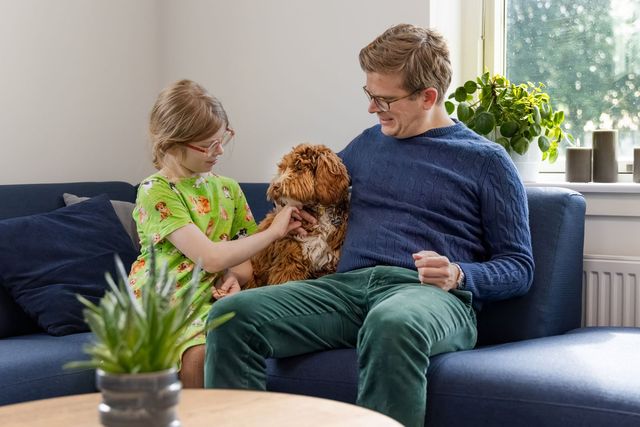 Hund, jente og mann som sitter i sofaen