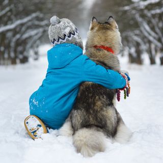 Et barn som holder rundt en hund ute i snøen