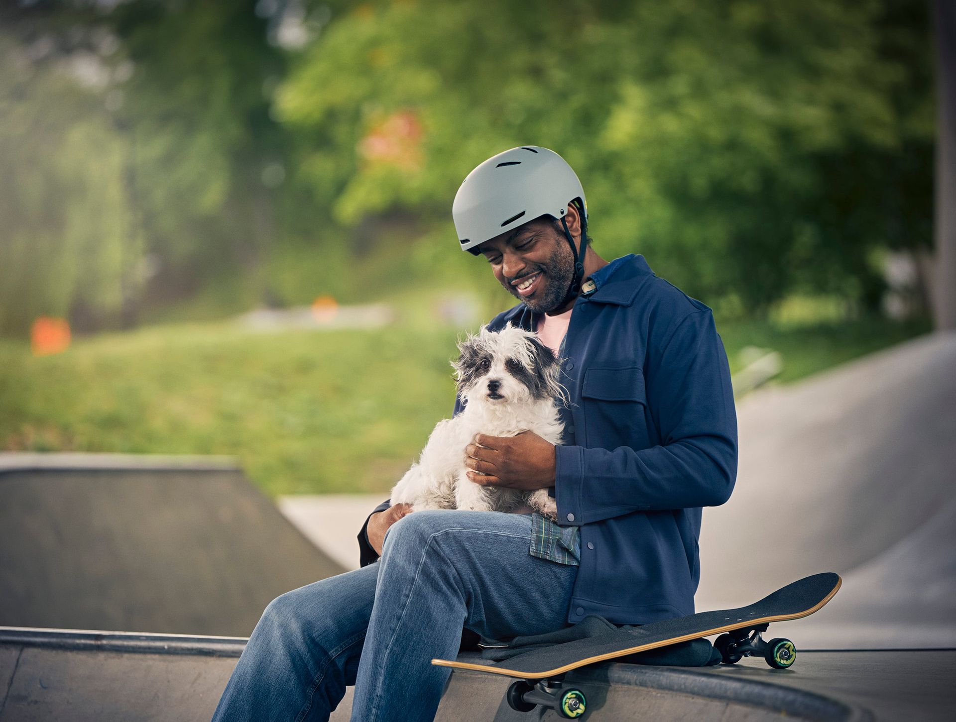 Man sitter i skatepark og holder en liten hund i fanget