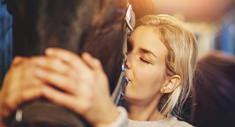 Kvinne koser med hest i stallen.