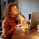 Dame og katt som sitter ved et bord med bærbar pc