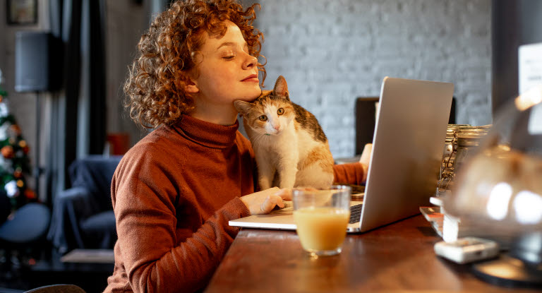 Dame og katt som sitter ved et bord med en bærbar pc 