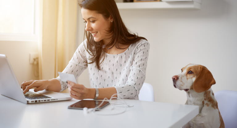 Dame sitter på PC med hund ved siden av