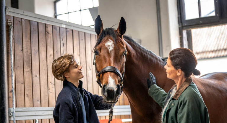 Gutt og dame står med en hest
